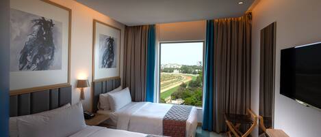 Habitación de hotel con dos camas, televisión, escritorio y vistas a un paisaje urbano.
