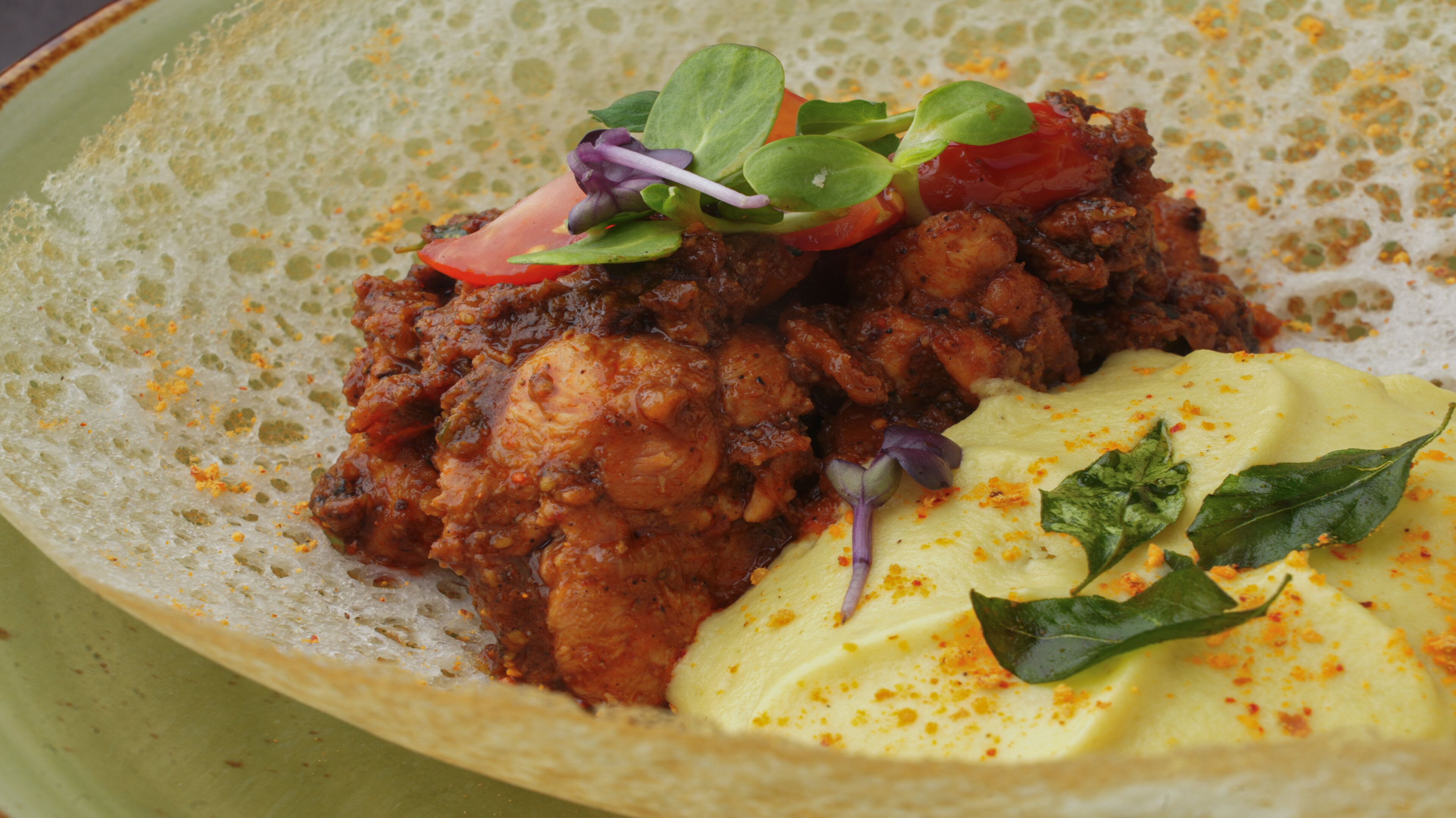 A plate with a dish of chicken curry, a dollop of yogurt, and some fresh vegetables.