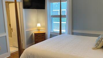 A bedroom with a bed, a nightstand, a lamp, a ceiling fan, a TV, and a window with a view of a balcony.