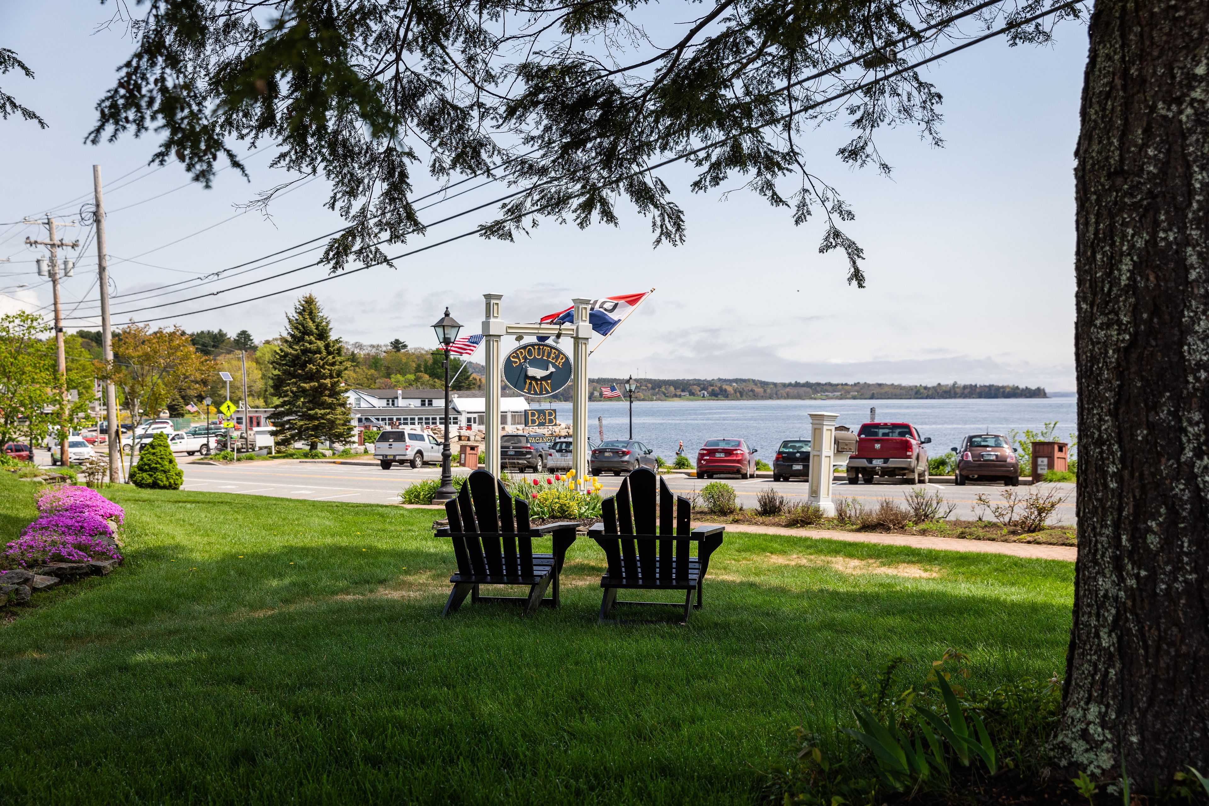 A sign for the Spouter Inn with a view of the water and parked cars.