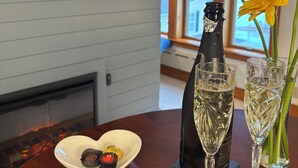 A table with a bottle, two glasses, a plate with chocolates, and a vase with flowers. - Spouter Inn Bed & Breakfast (Lincolnville)