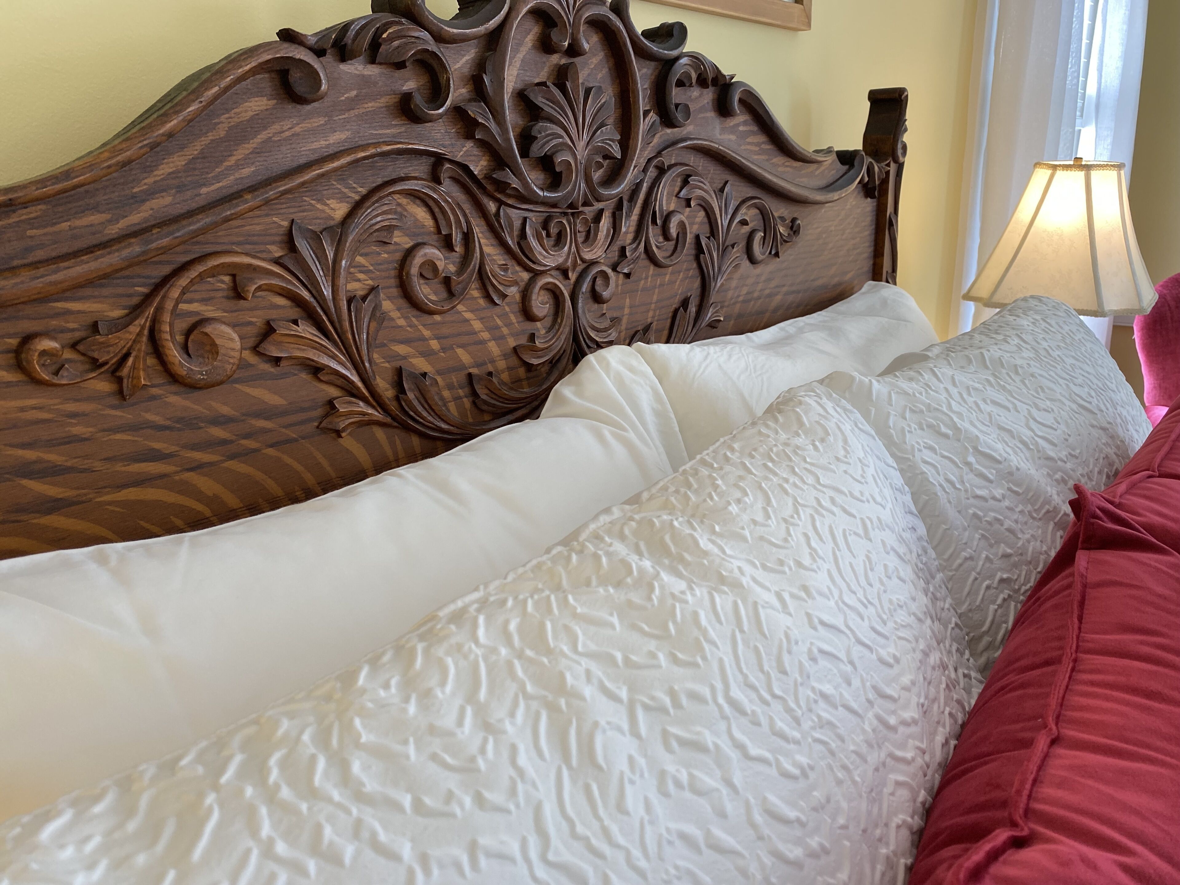 Een bed met een houten hoofdbord, witte kussens en een rode deken.