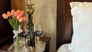 A wooden nightstand with a lamp, a tray holding wine glasses, a bottle, and a vase with pink tulips.