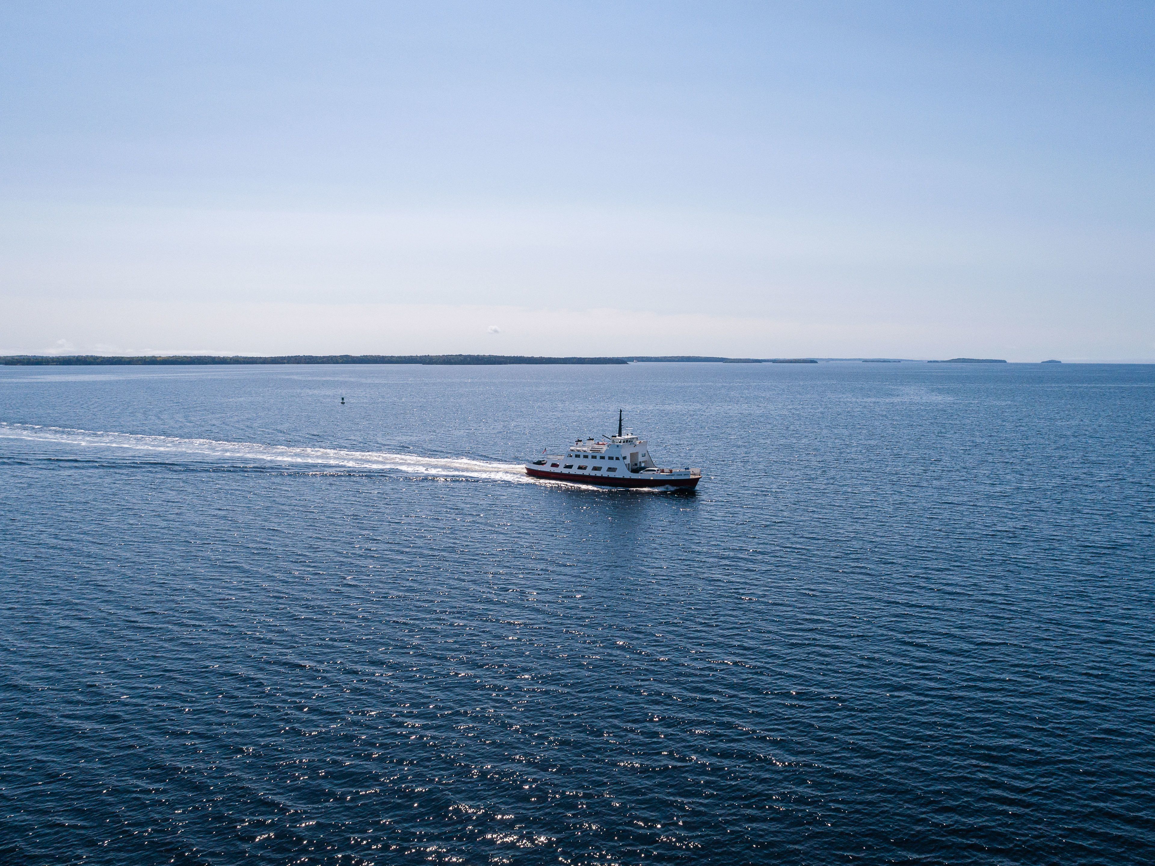 Un barco navega sobre un mar tranquilo, con tierra a lo lejos en el horizonte.
