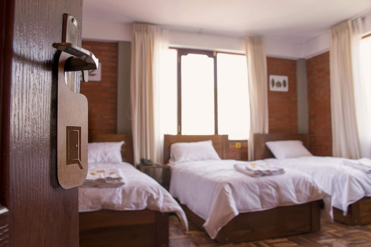 A hotel room with two beds, a wooden door, and a window with curtains.
