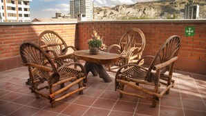 A terrace with wicker chairs and a table, a brick wall, and a view of buildings and mountains. - Qhini Hotel Boutique (La Paz)
