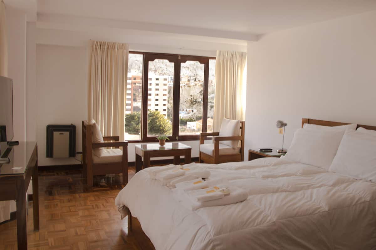 A hotel room with a large bed, a desk, a chair, and a window with curtains.