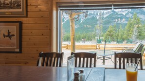 A wooden interior with a table and chairs, a window with a mountain view, and a framed picture on the wall. - David Thompson Resort Hotel (Cline River)