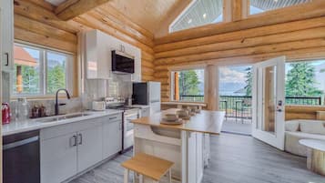 A modern log cabin with a kitchen, dining area, and a balcony with a view of the mountains.