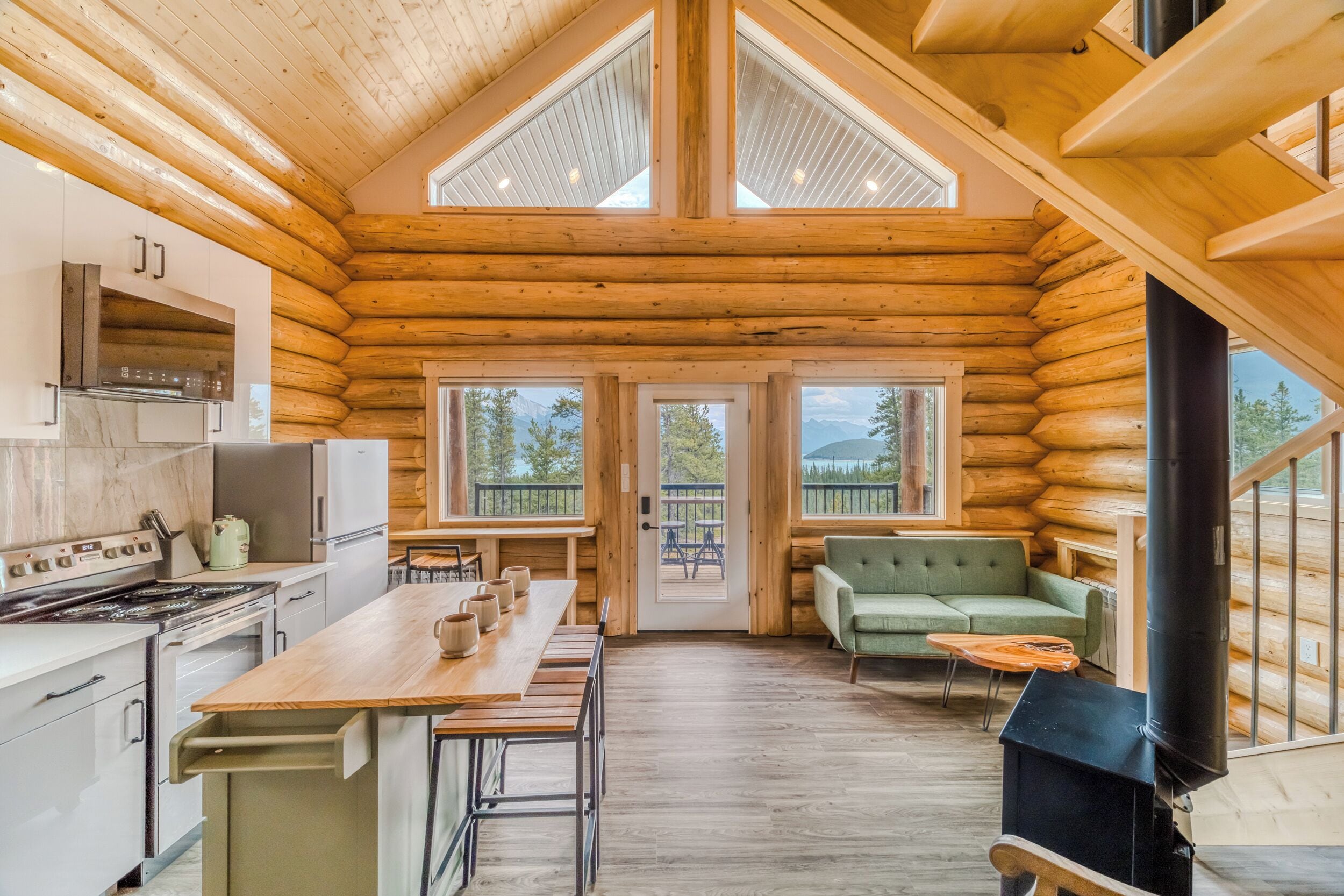 A log cabin interior with a kitchen, dining area, and a living room with a sofa and a fireplace.