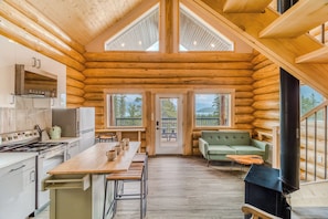 A log cabin interior with a kitchen, dining area, and a living room with a sofa and a fireplace. - David Thompson Resort Hotel (Cline River)