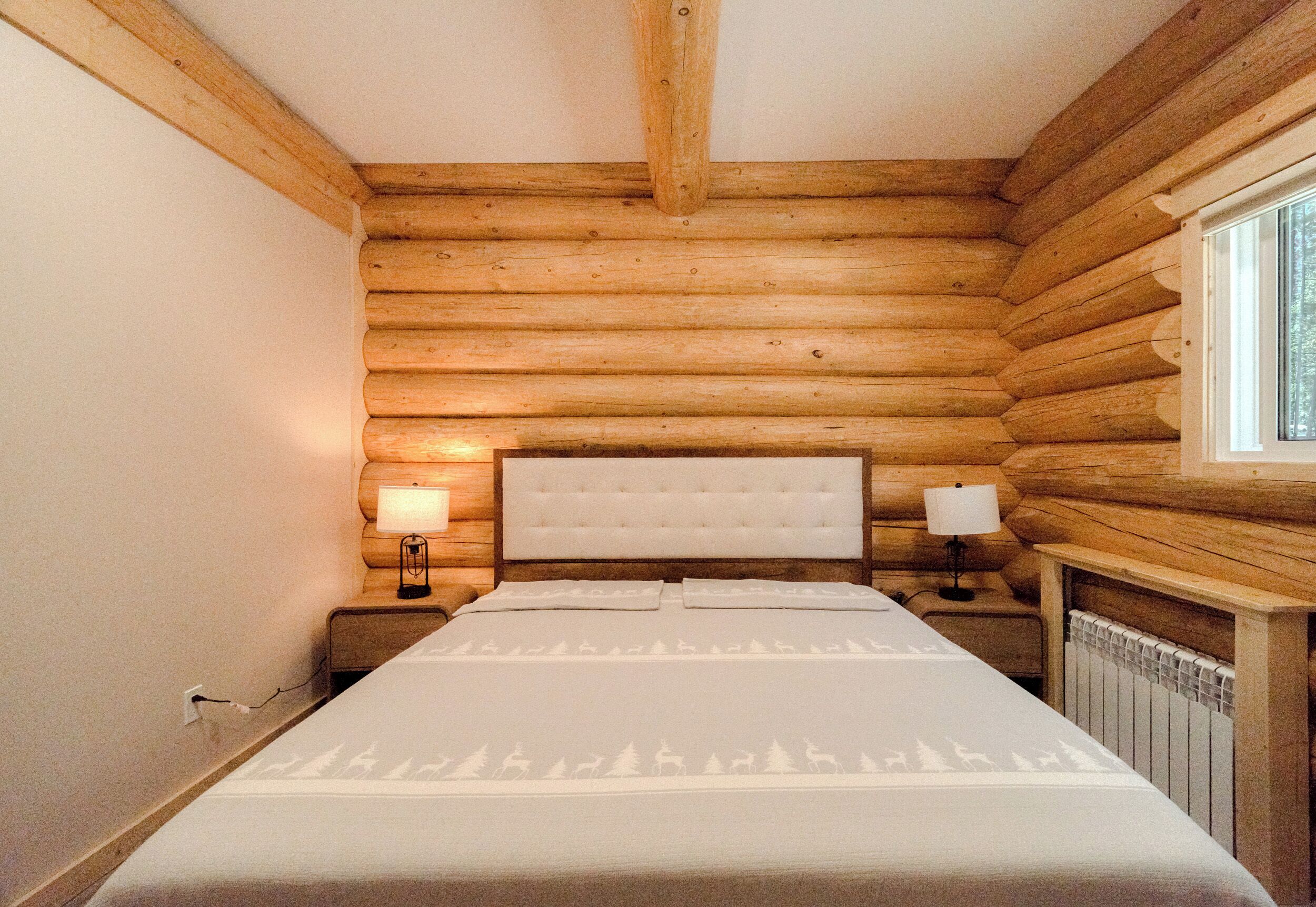 A log cabin bedroom with a bed, two bedside lamps, and a window.
