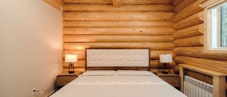 A log cabin bedroom with a bed, two bedside lamps, and a window.