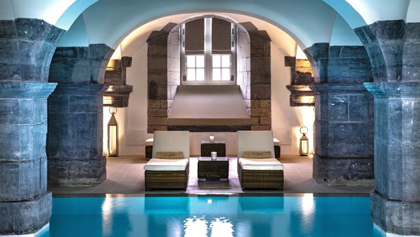 Un área de piscina con columnas de piedra, dos sillones de descanso y una chimenea de piedra.
