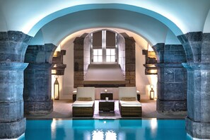 A pool area with stone columns, two lounge chairs, and a stone fireplace. - Royal Hainaut Spa & Resort Hotel (Valenciennes)