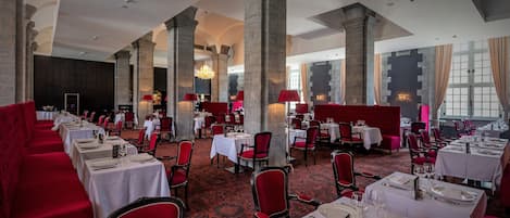Un comedor elegante con asientos tapizados en rojo, manteles blancos y sillas rojas.