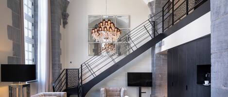 A spacious living area with a grand staircase, a chandelier, and modern furnishings.