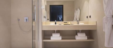 Un baño moderno con cabina de ducha de vidrio, tocador doble y una bata colgada en la pared.