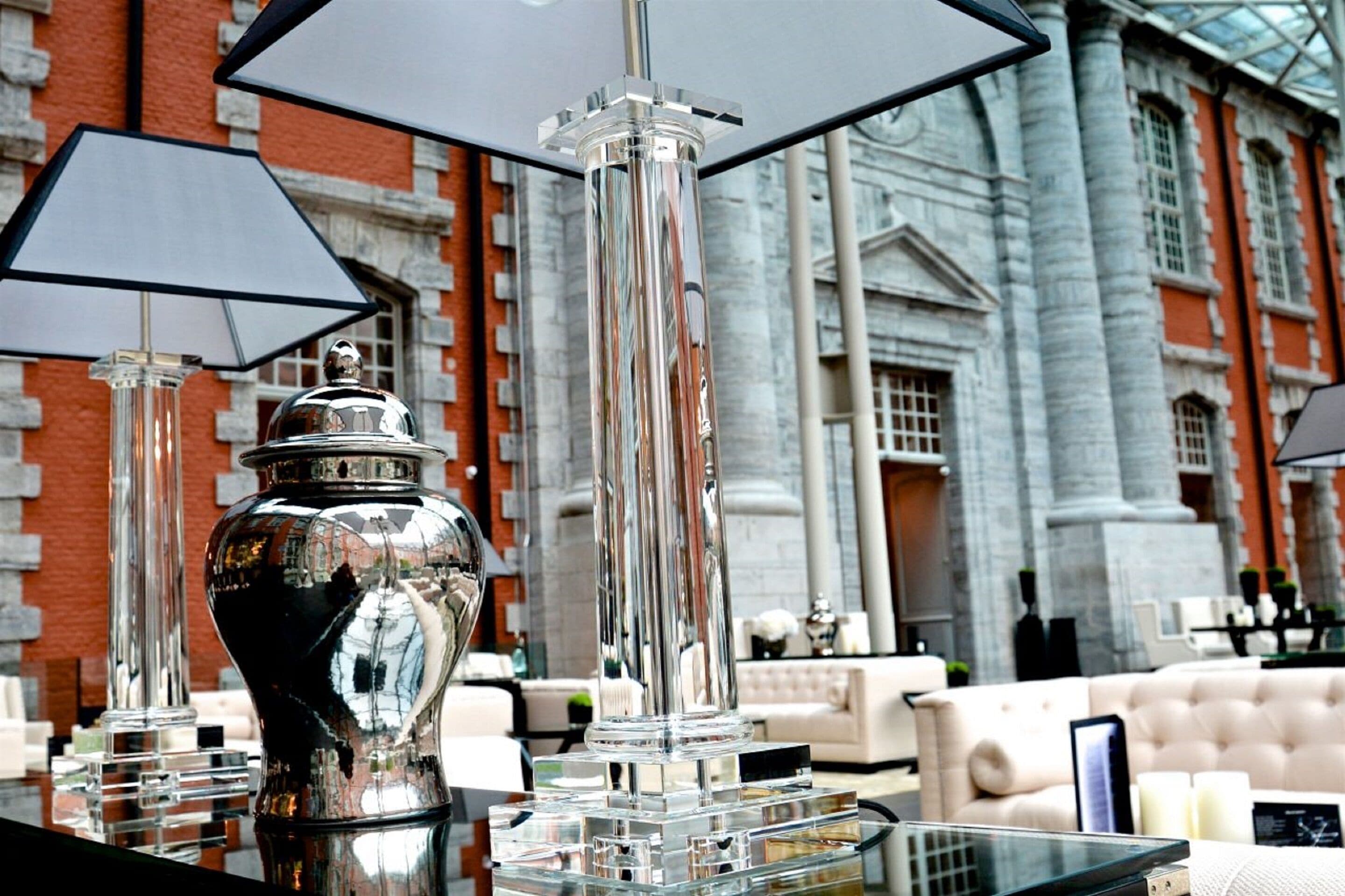 A luxurious interior with a glass table, a silver vase, and a modern lamp.
