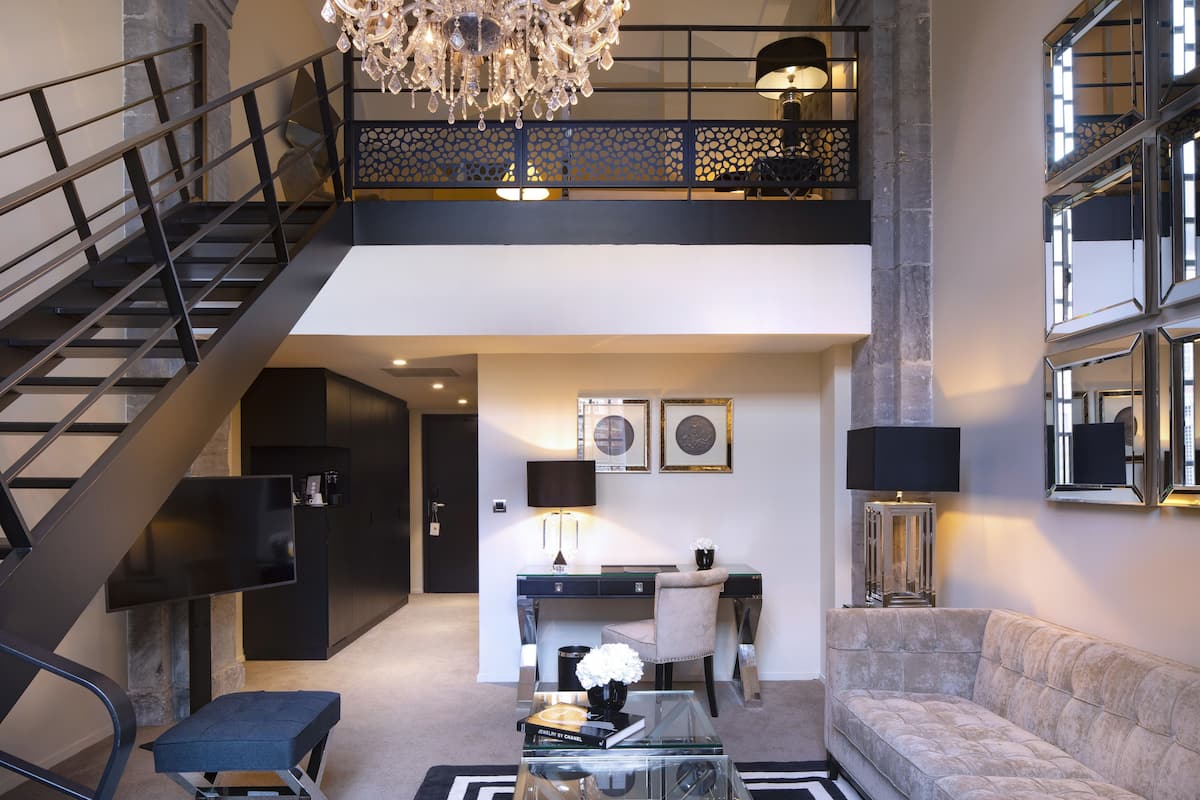 A modern living room with a staircase, a desk, a sofa, and a chandelier.