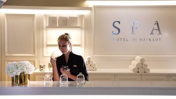 Un espace d’accueil avec une enseigne indiquant « SPA HOTEL DU HAINAUT » et une femme tenant un verre.
