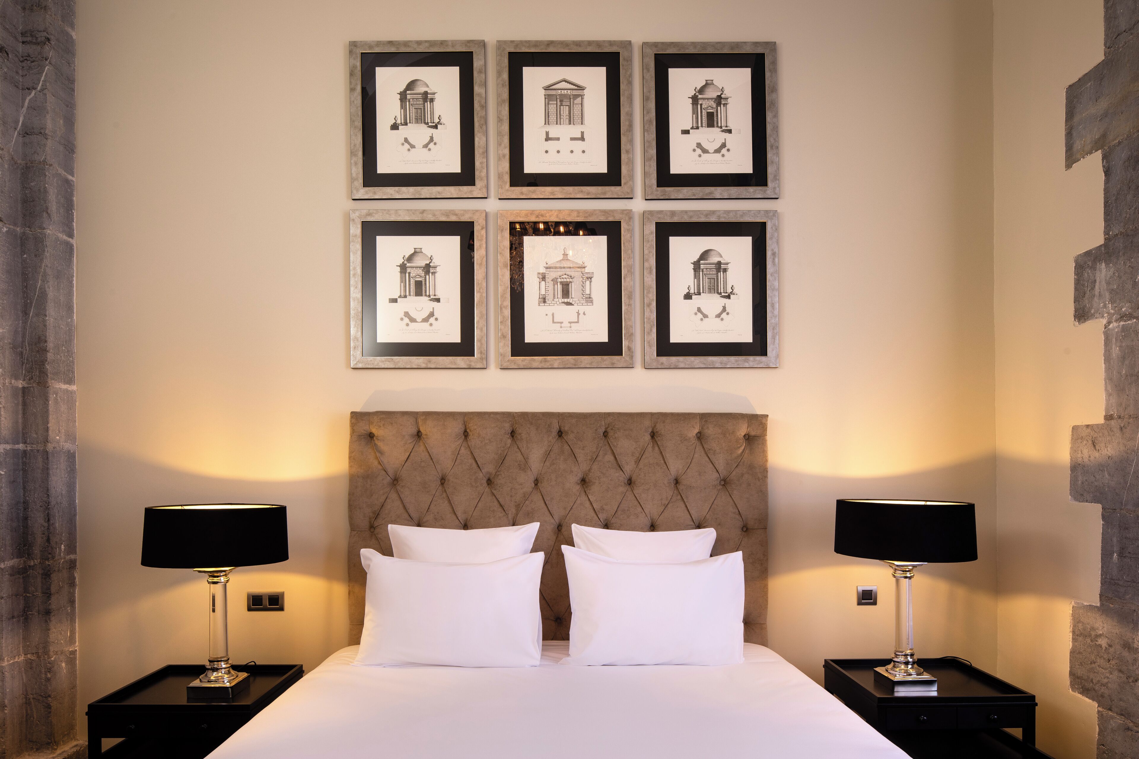 Een hotelkamer met een groot bed, twee nachtkastjes met lampen en zes ingelijste foto's aan de muur.