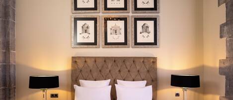 Una habitación de hotel con una cama grande, dos mesitas de noche con lámparas y seis cuadros enmarcados en la pared.