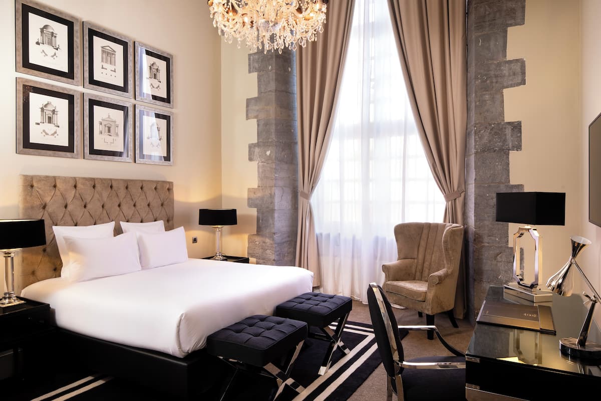 A hotel room with a large bed, a chair, a desk, and a chandelier.