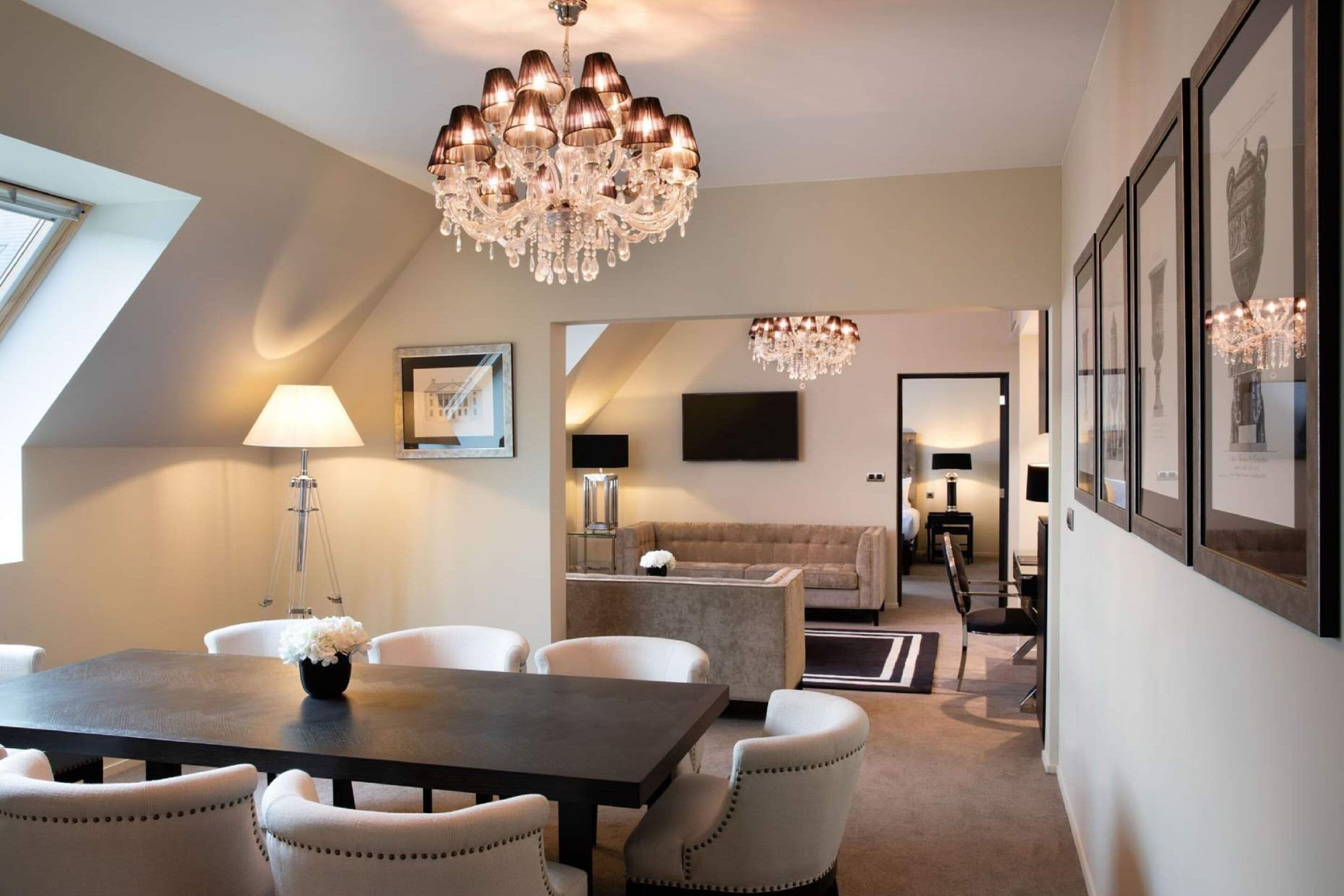 A modern dining area with a dark wooden table, white upholstered chairs, and a chandelier.