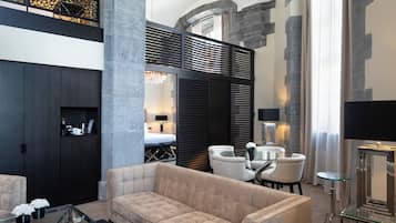 A modern hotel lobby with a plush beige sofa, a glass coffee table, and a seating area with white chairs.