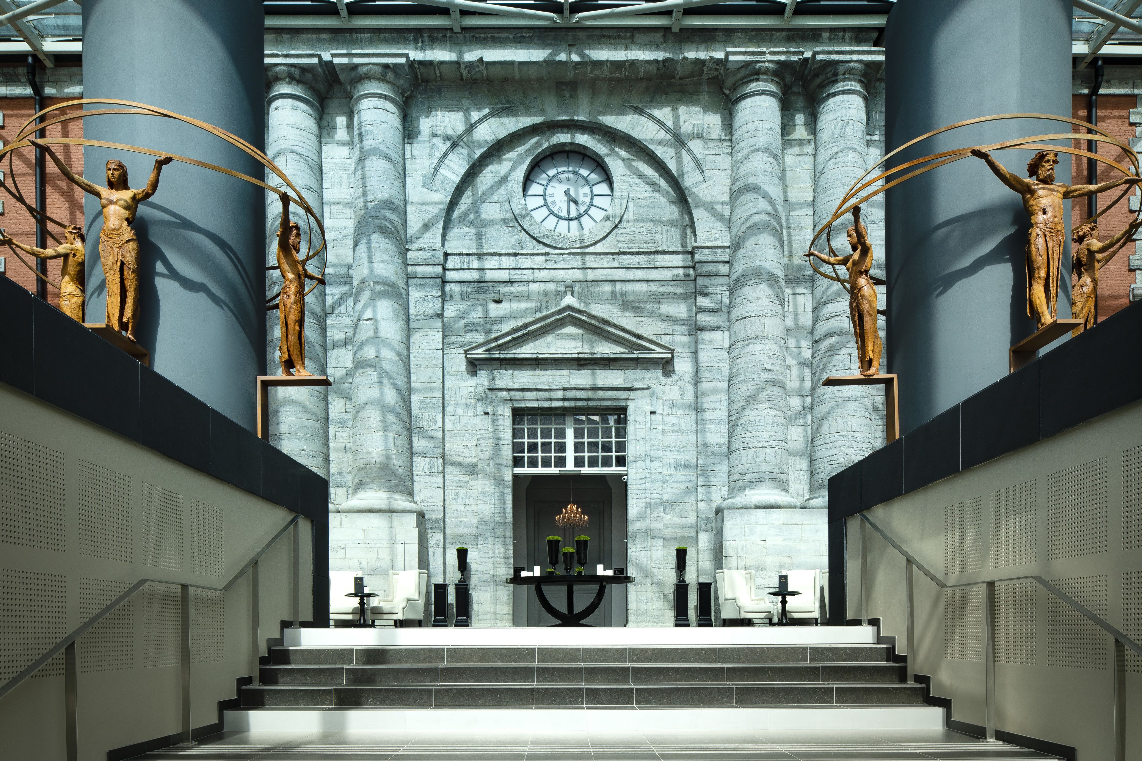 Un'imponente ingresso con un orologio grande, statue e una scalinata che conduce a un piano superiore.