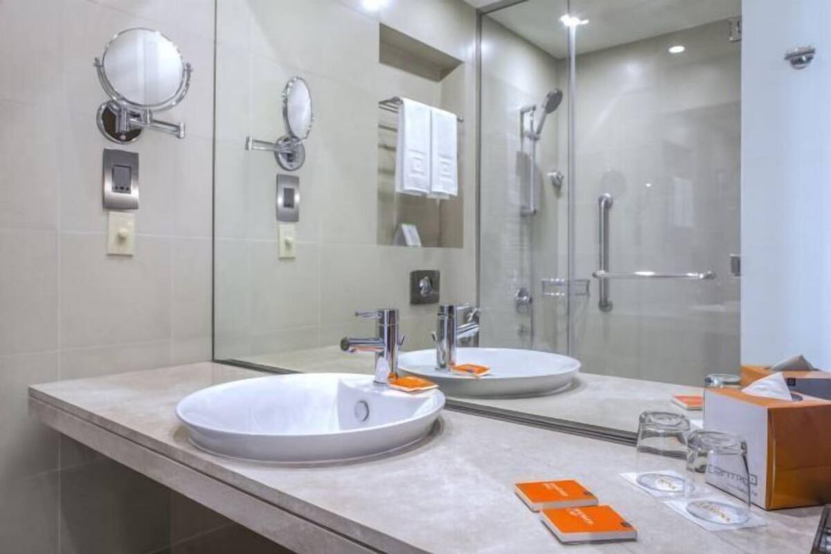Uma casa de banho moderna com um espelho grande, uma pia e um compartimento de chuveiro em vidro.