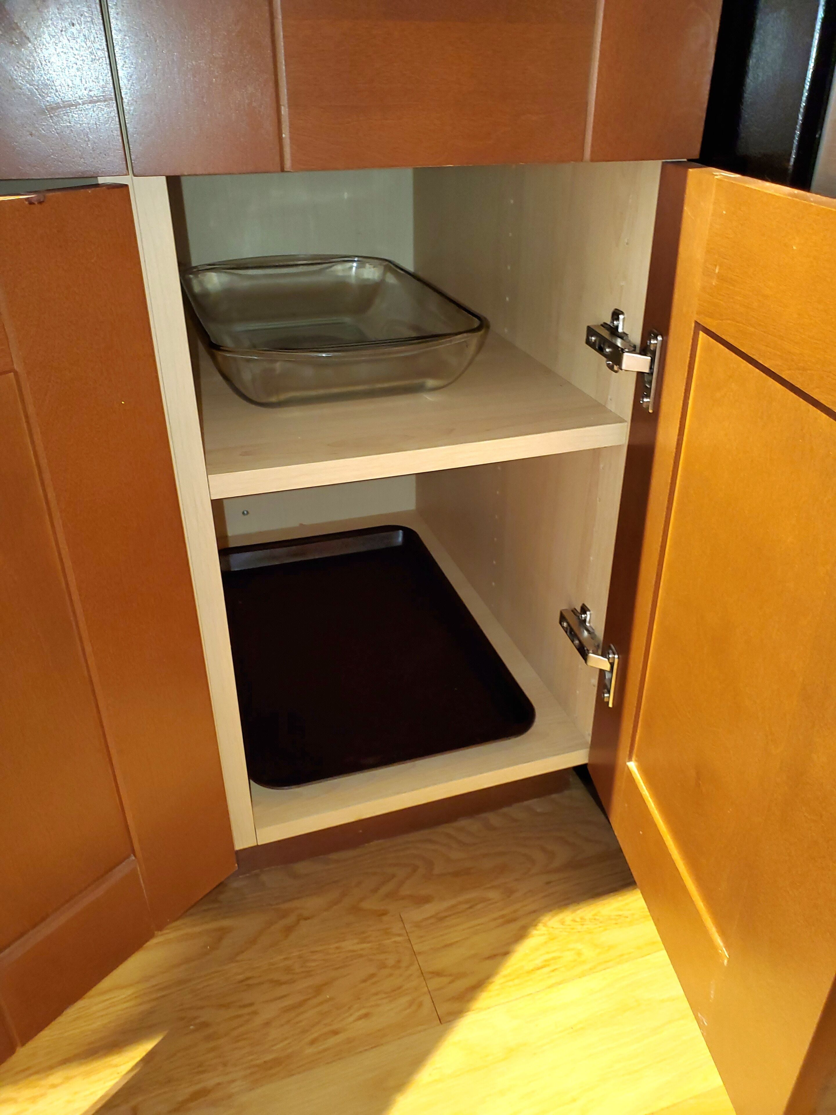 Una cocina con armarios de madera, un recipiente de vidrio para hornear en el estante superior y una bandeja negra en el estante inferior.
