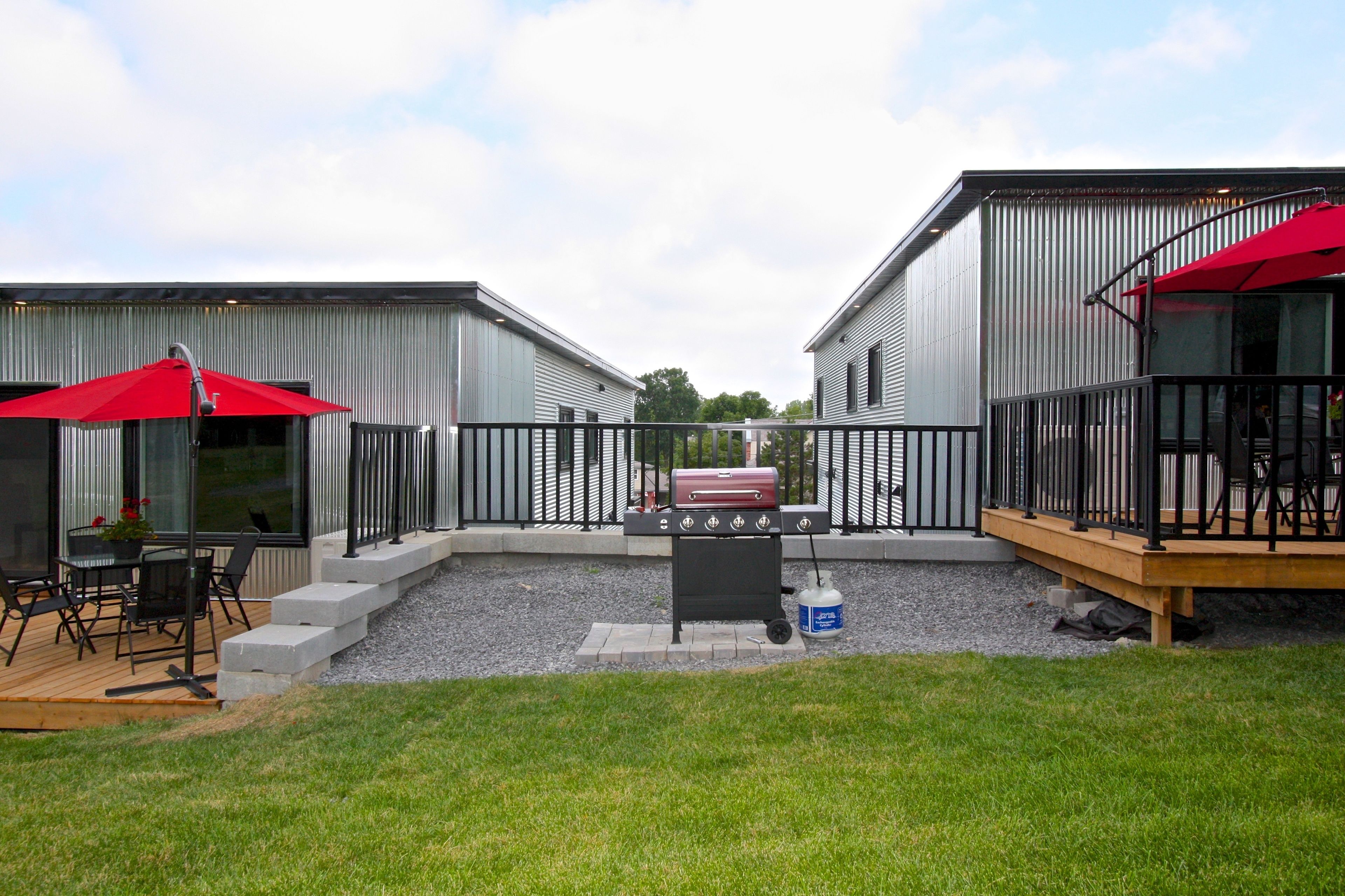 A modern outdoor patio with a barbecue grill, seating area, and red umbrellas.