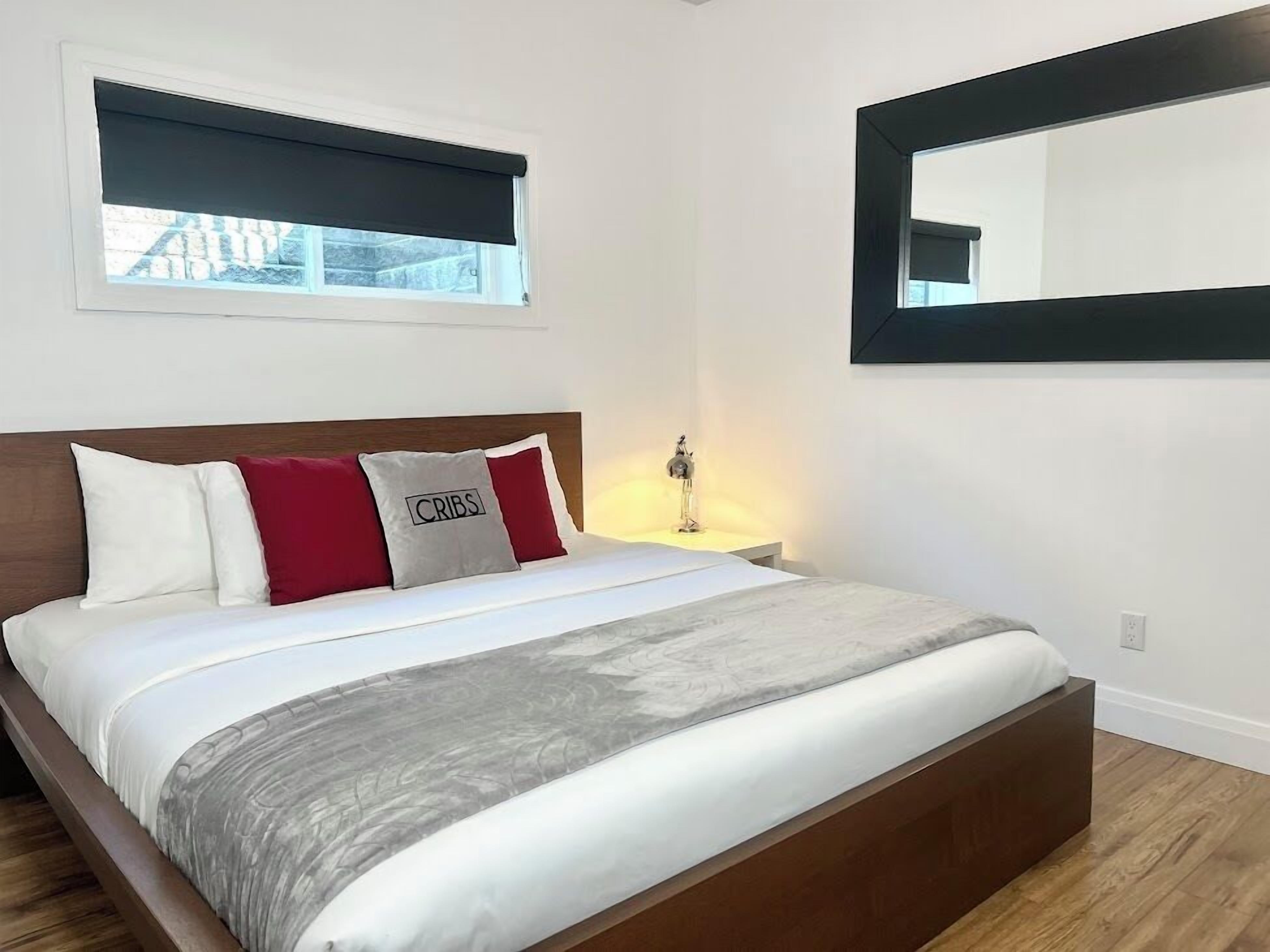 Une chambre à coucher comprenant un lit, une table de chevet, une lampe, une fenêtre avec un store et un miroir sur le mur.