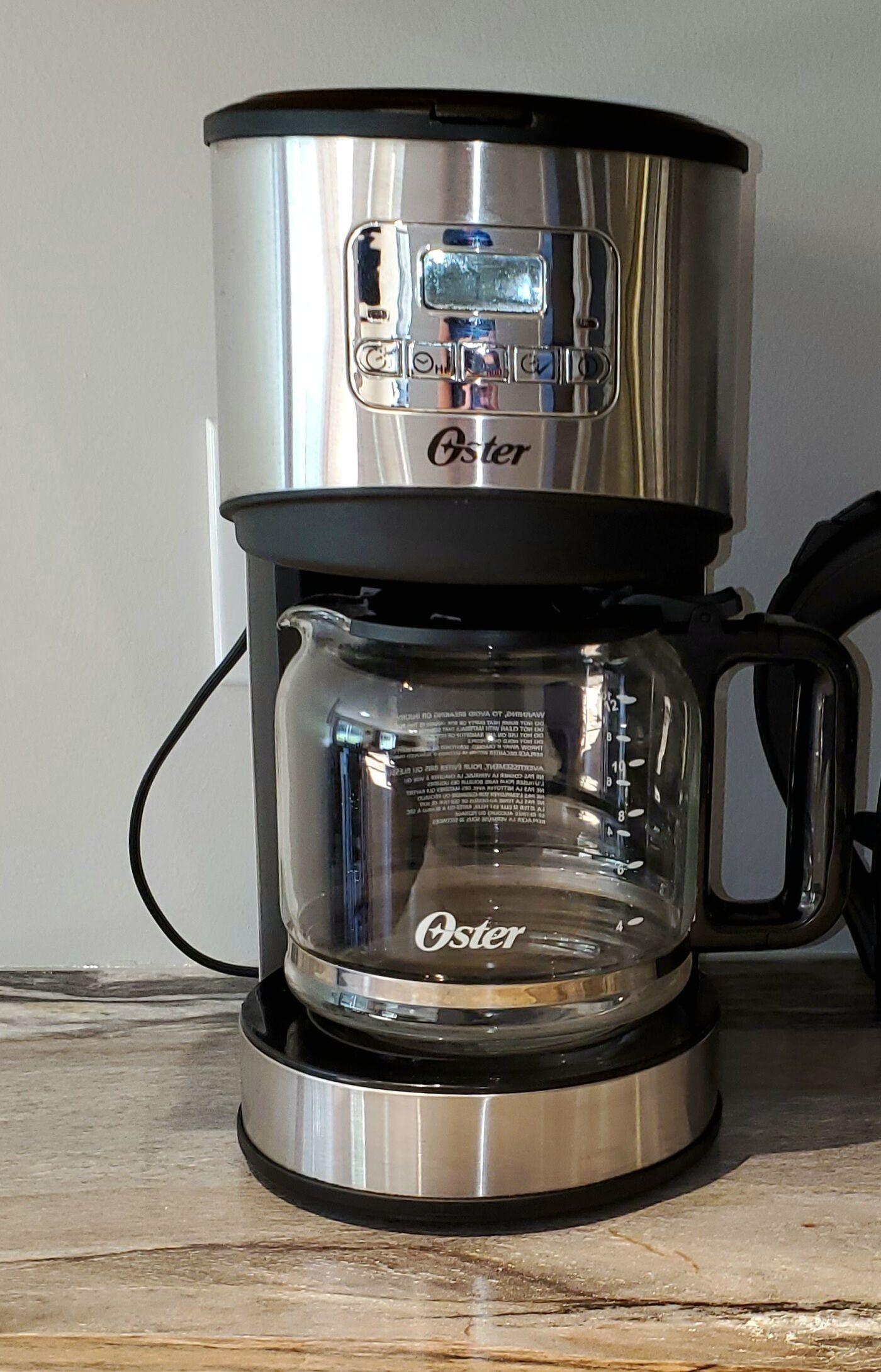 Una cafetera Oster de acero inoxidable con jarra de vidrio y asa negra.