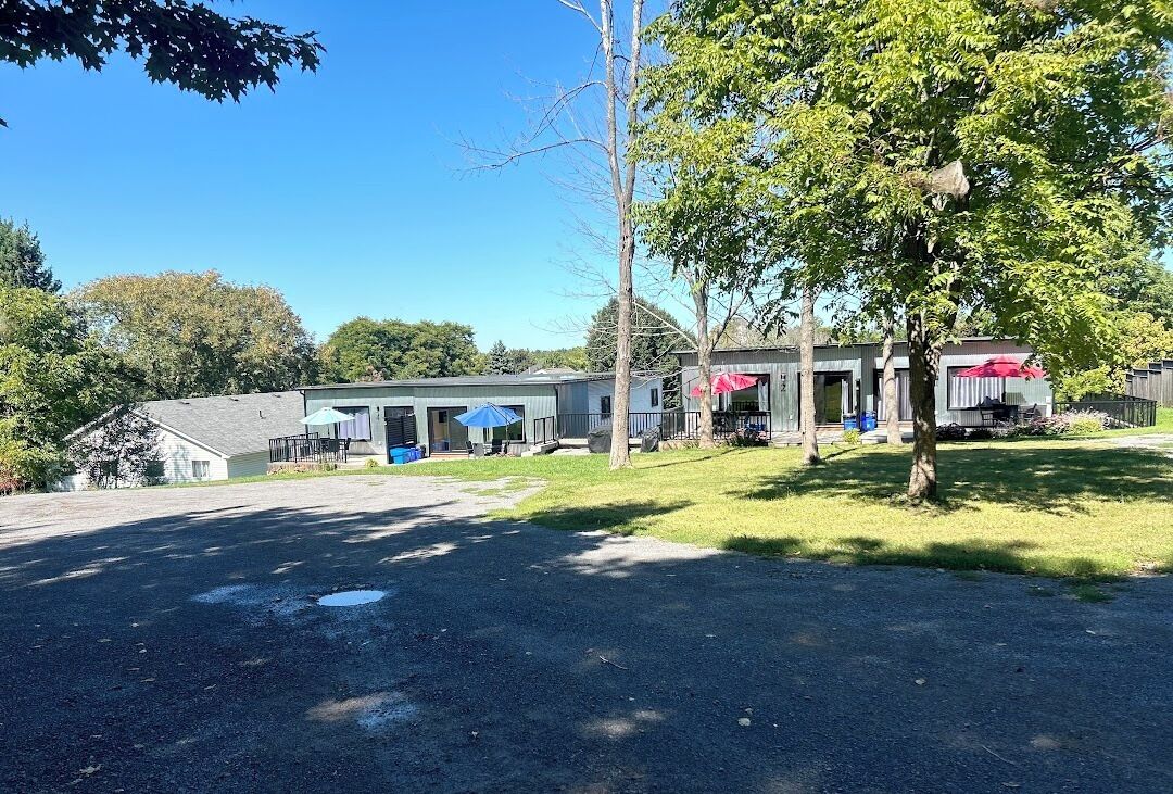 Een gebouw met een overdekt terras, een parkeerplaats en bomen.