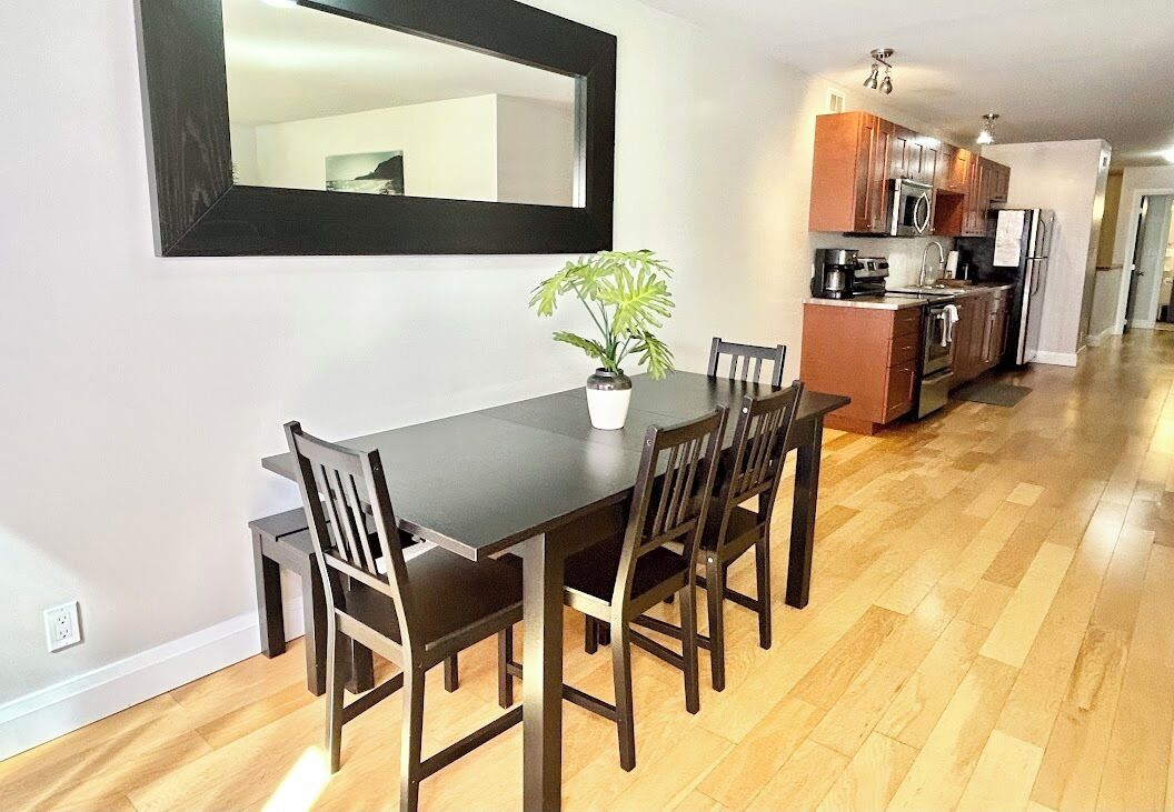 A dining area with a dark wooden table and chairs, a potted plant, and a large mirror on the wall.