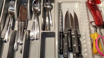 Un cajón con diversos utensilios y herramientas de cocina, como tenedores, cuchillos, cucharas y un afilador de cuchillos con mango rojo.