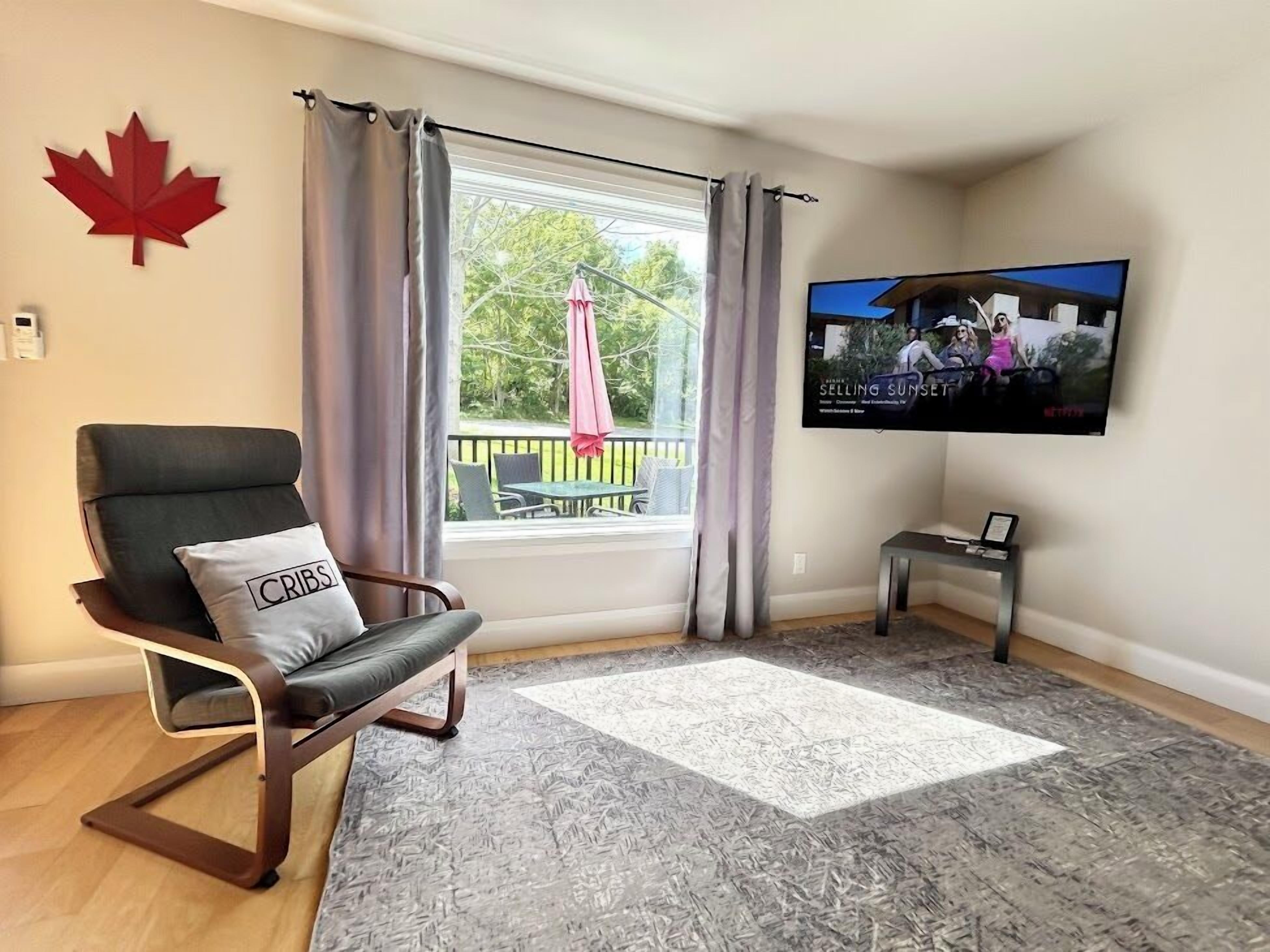 A living room with a large window, a TV, a chair, and a small table.