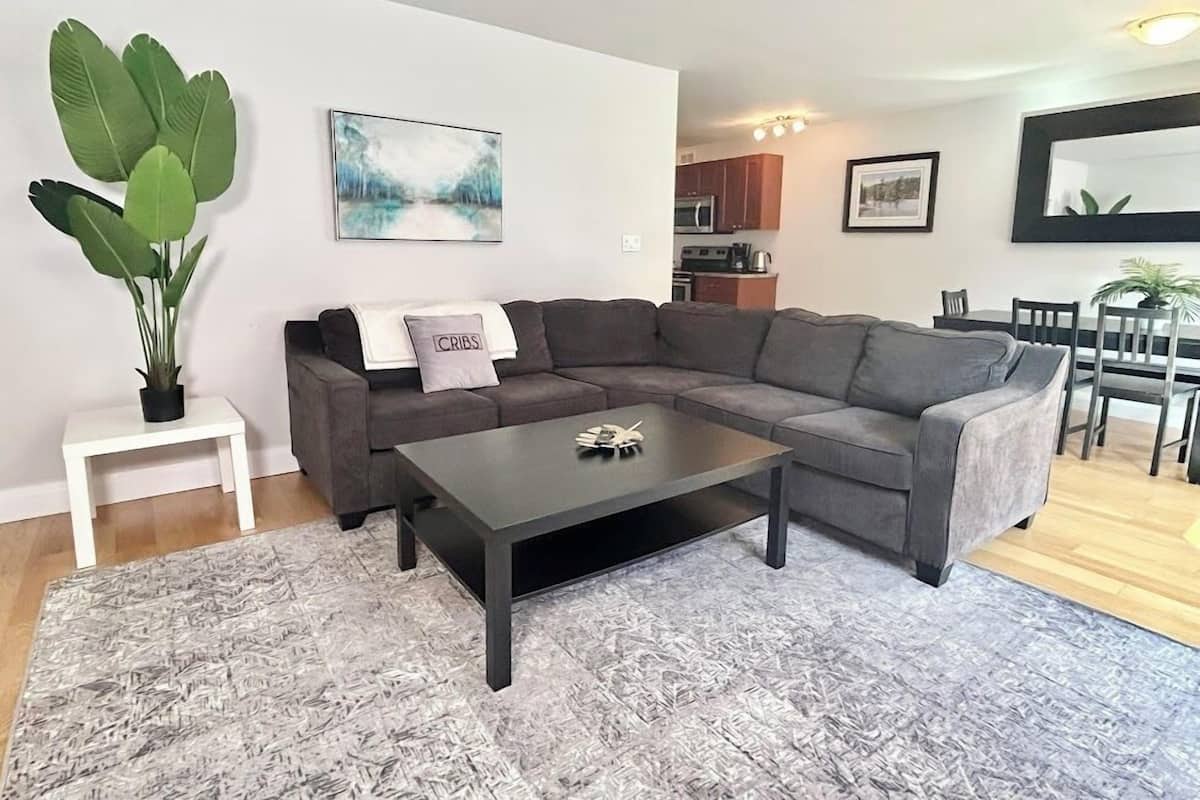 Ein modernes Wohnzimmer mit einer Eckcouch, einem Couchtisch und einer großen Topfpflanze.
