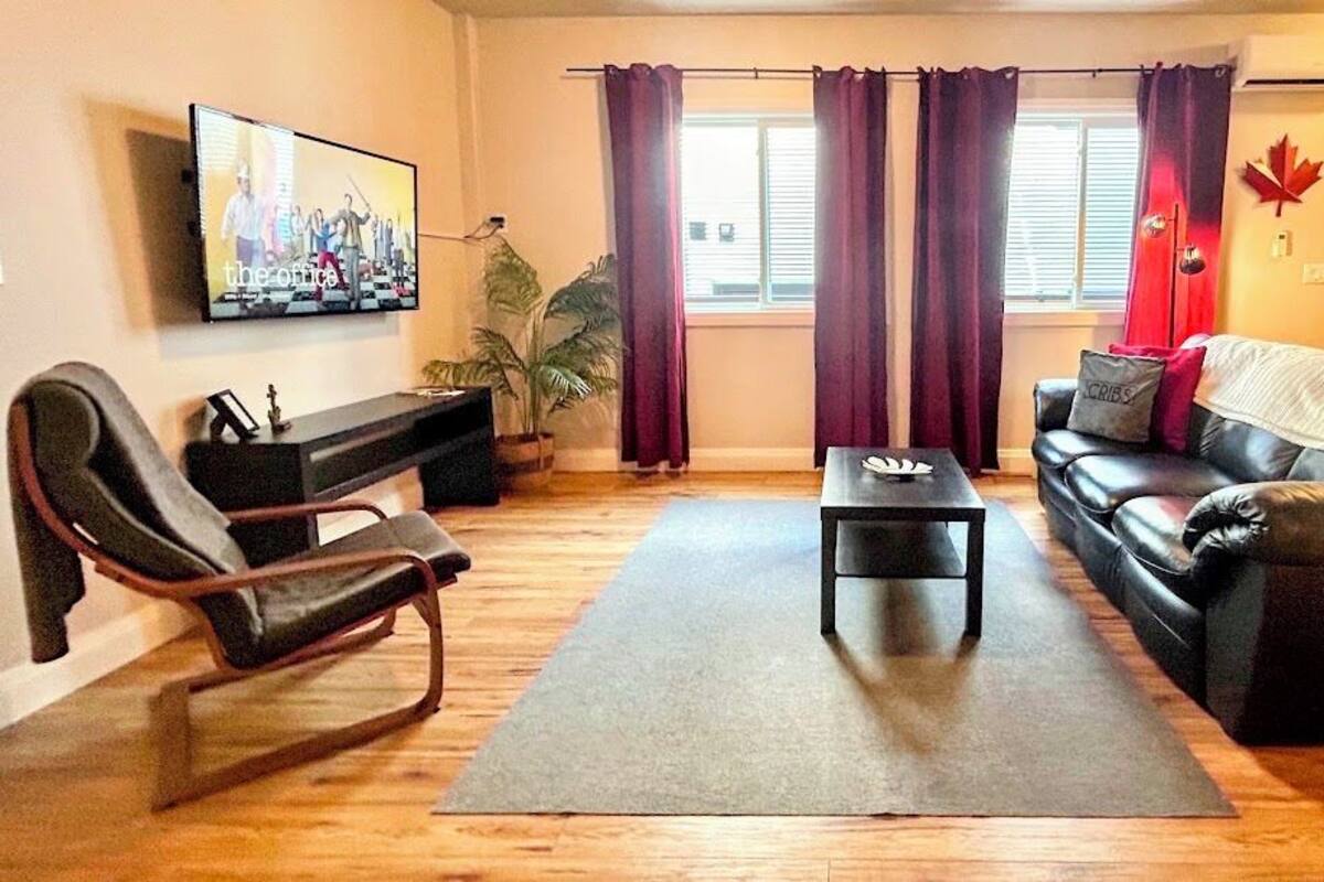 Ein Wohnzimmer mit einer Couch, einem Sessel, einem Couchtisch und einem Fernseher an der Wand.