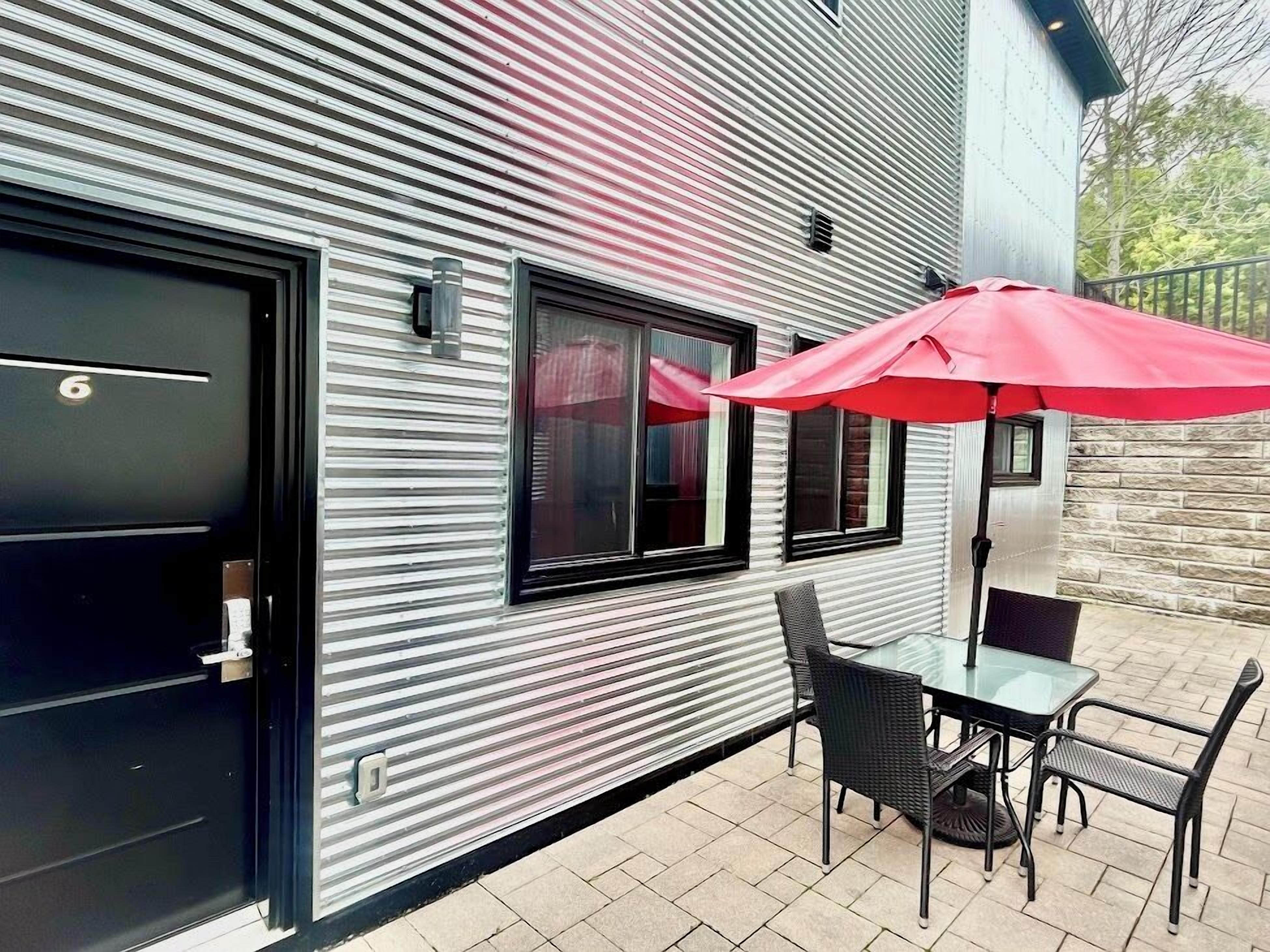 Un bâtiment moderne à la façade métallique, doté d’une porte noire et d’un patio aménagé avec une table et des chaises.