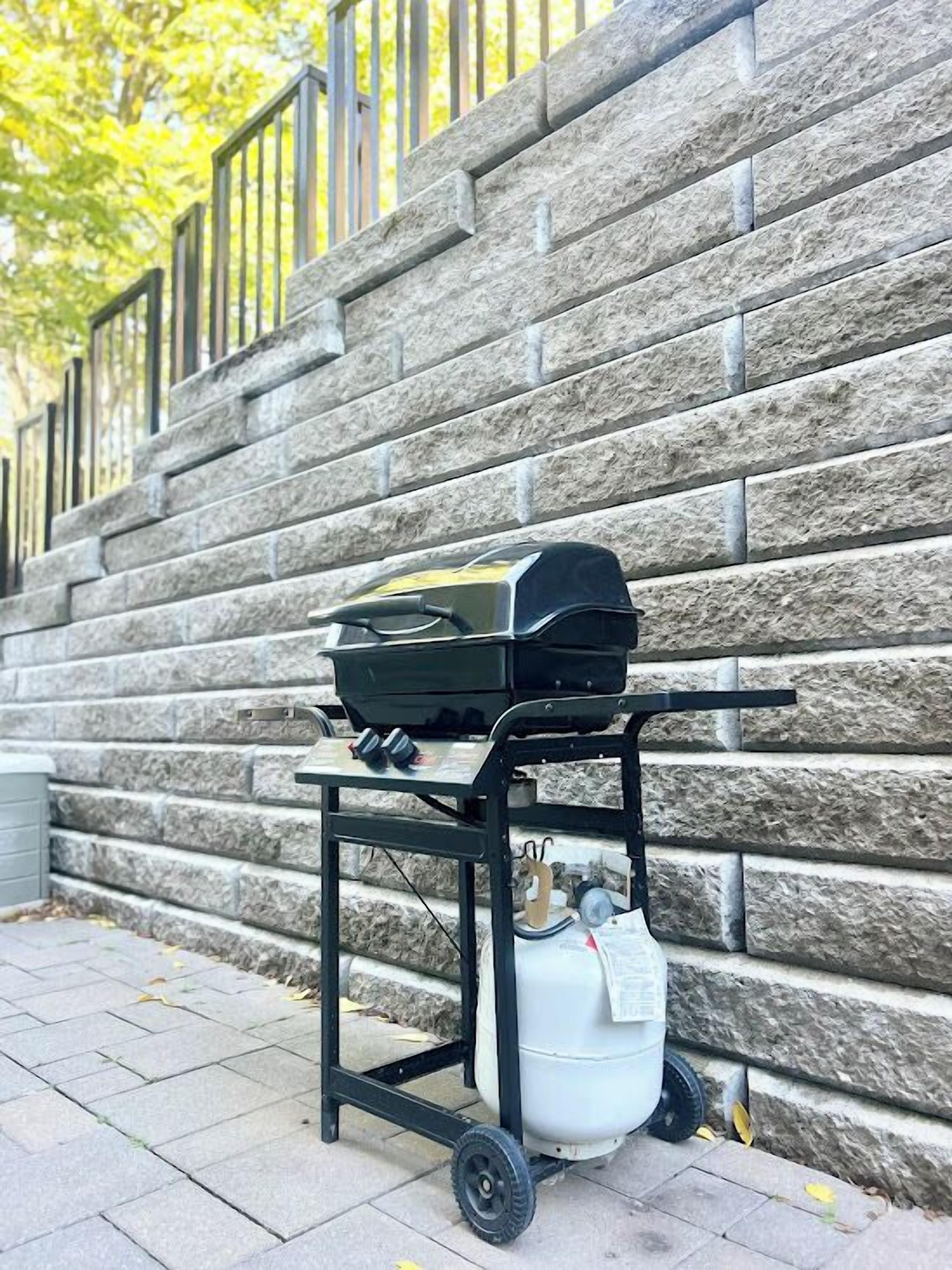 A portable grill on a wheeled cart against a stone wall.