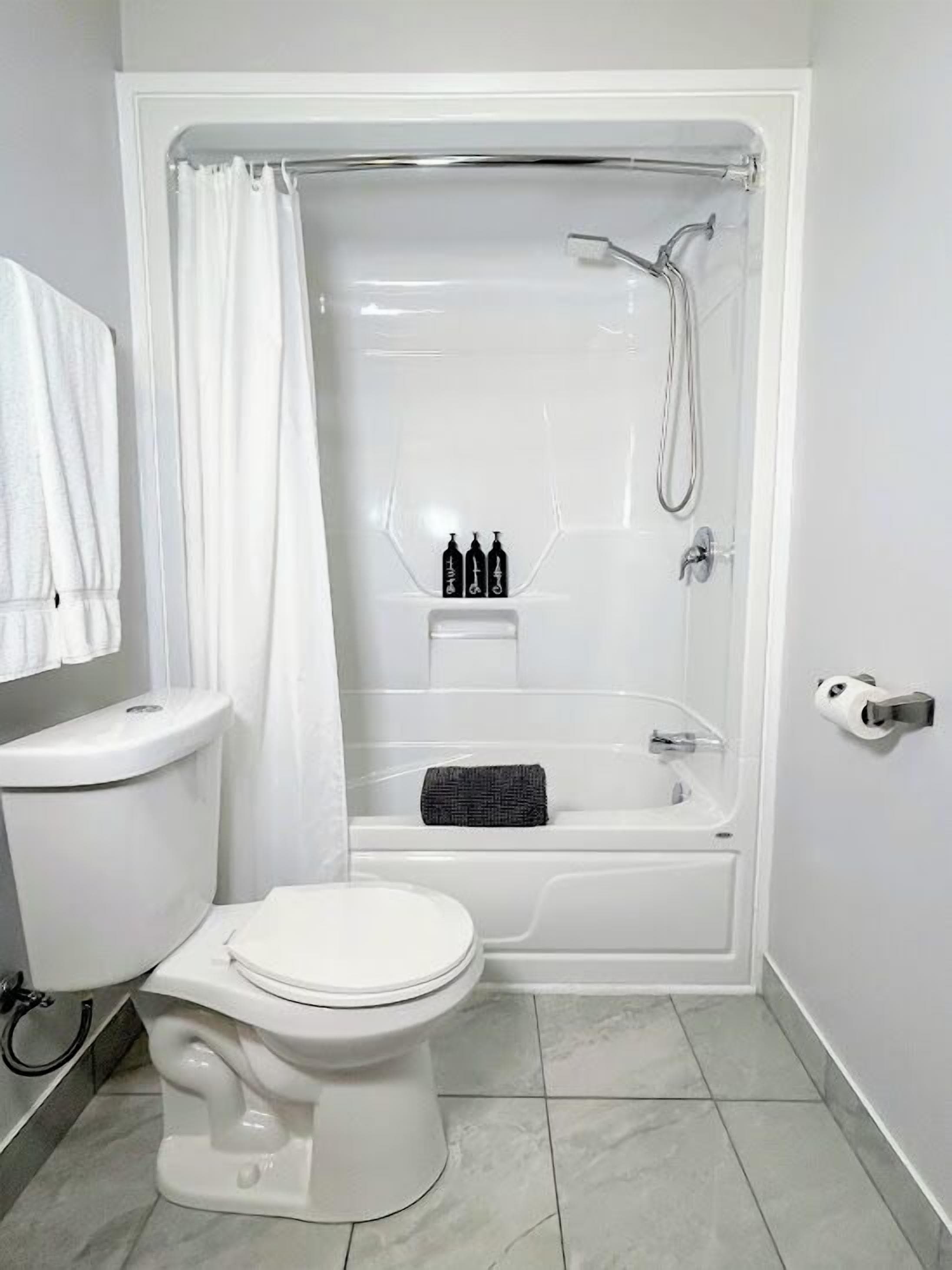 A bathroom with a toilet, a bathtub, and a shower. There is a towel rack and a toilet paper holder.