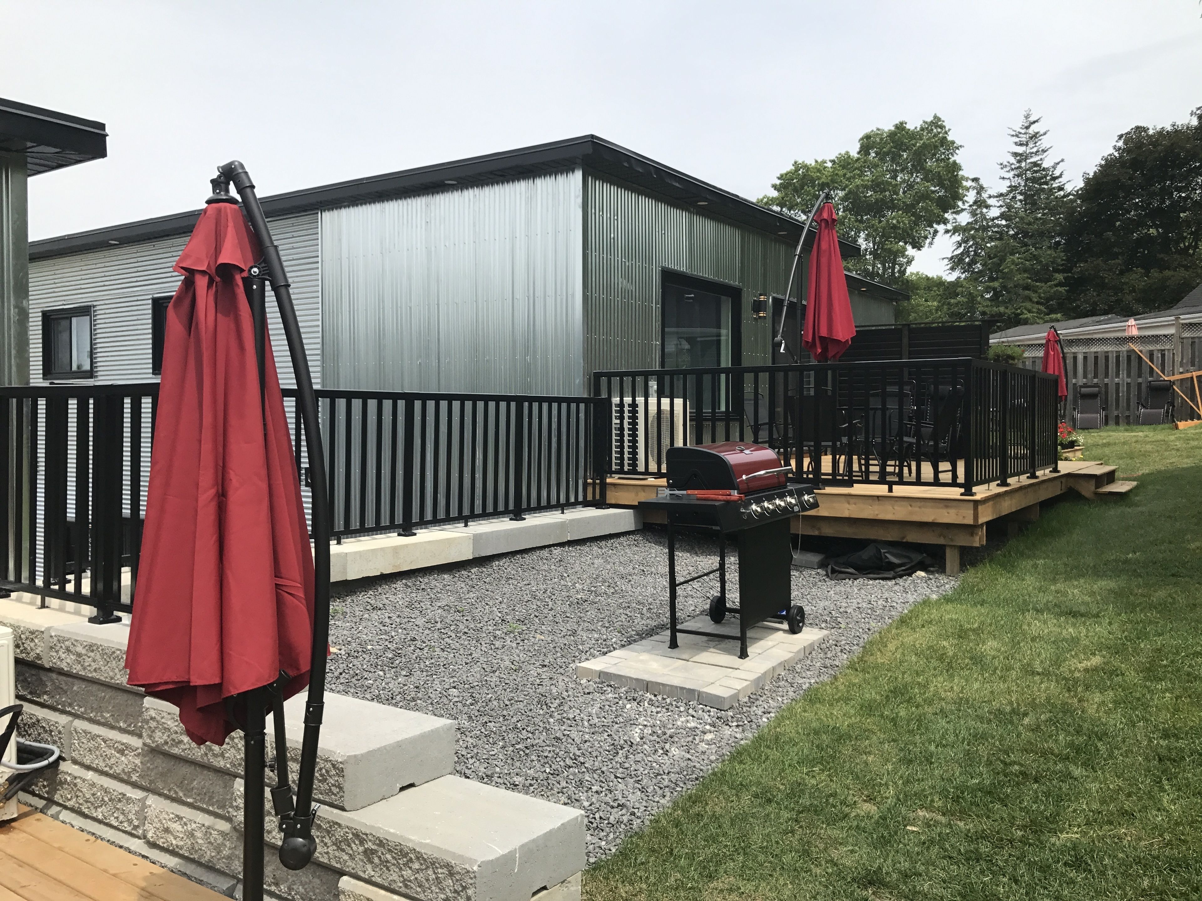 A patio area with a barbecue grill, outdoor seating, and a metal building in the background.
