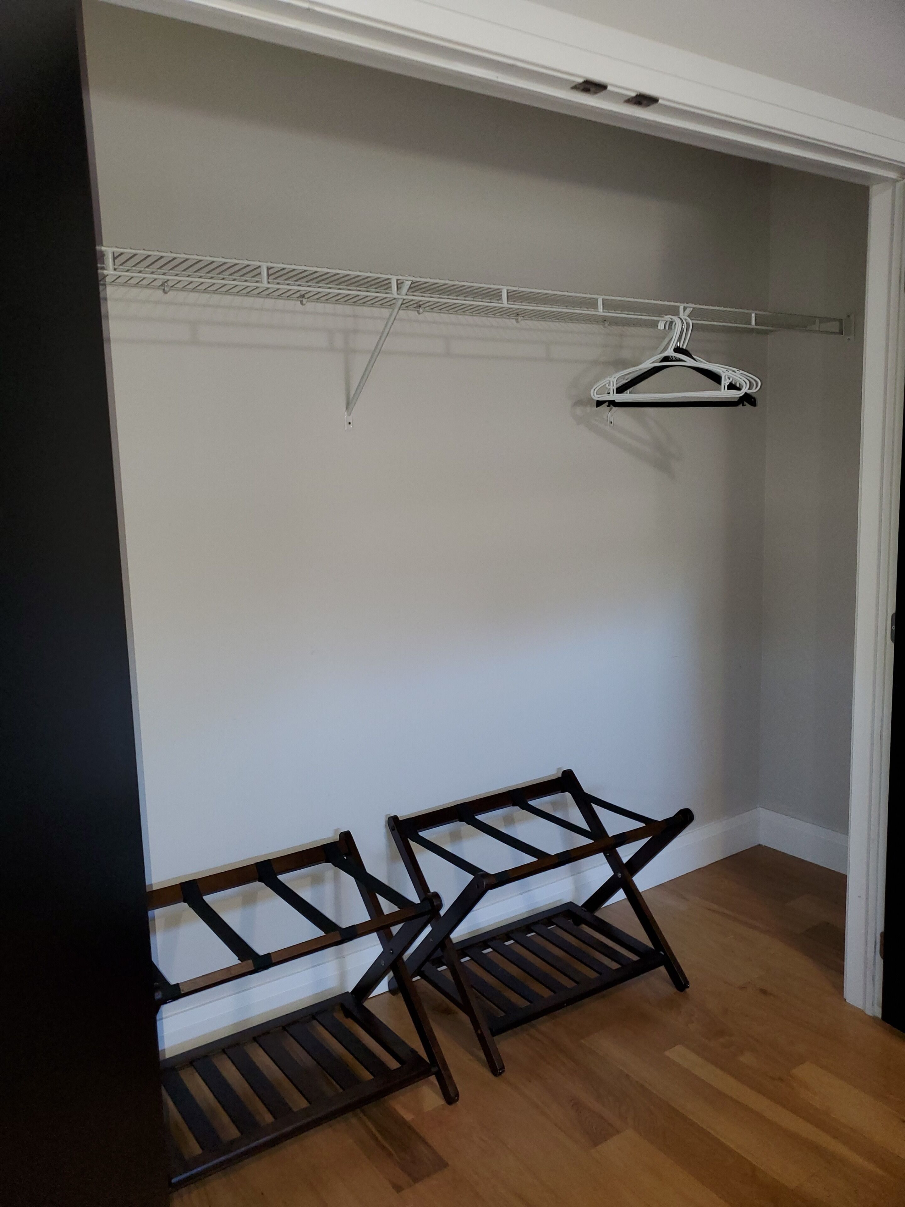 A walk-in closet with a wooden bench, a white hanging rod, and a white hanger.