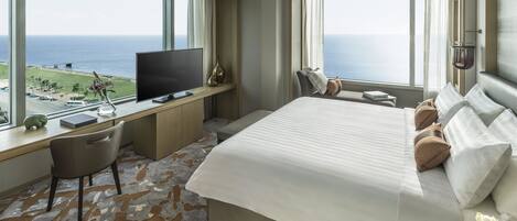 Une chambre d’hôtel avec un grand lit, un bureau avec une télévision et une vue sur l’océan.