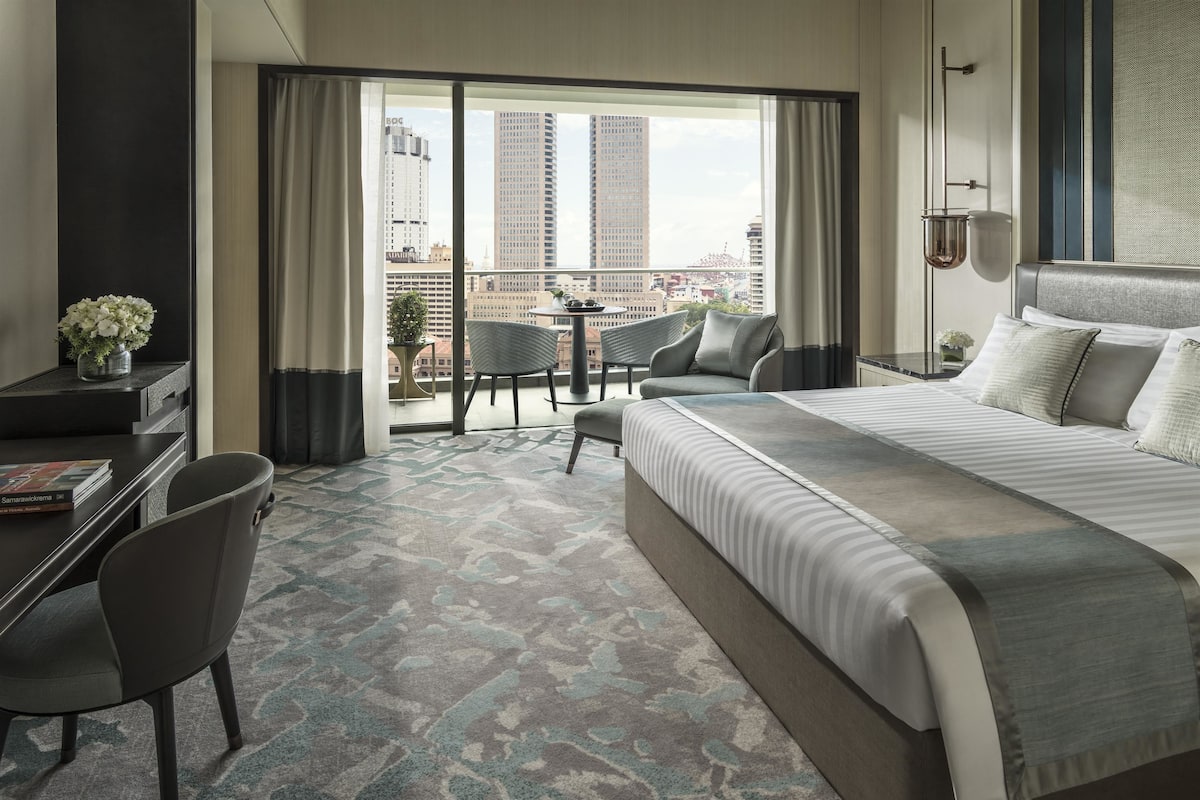 Une chambre d’hôtel avec un grand lit, un bureau, une chaise et un balcon offrant une vue sur le panorama de la ville.