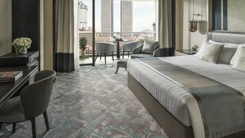 A hotel room with a large bed, a desk, a chair, a balcony with a view of the city skyline.
